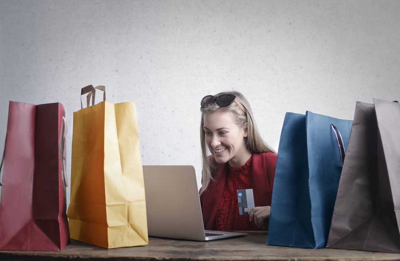 A woman sitting infront of a laptop with allot of shopping bags around her.